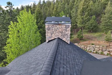Finished asphalt shingle roof around a stone chimney